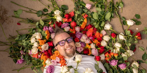 Man lying on floor with different colored roses around his head and face. 