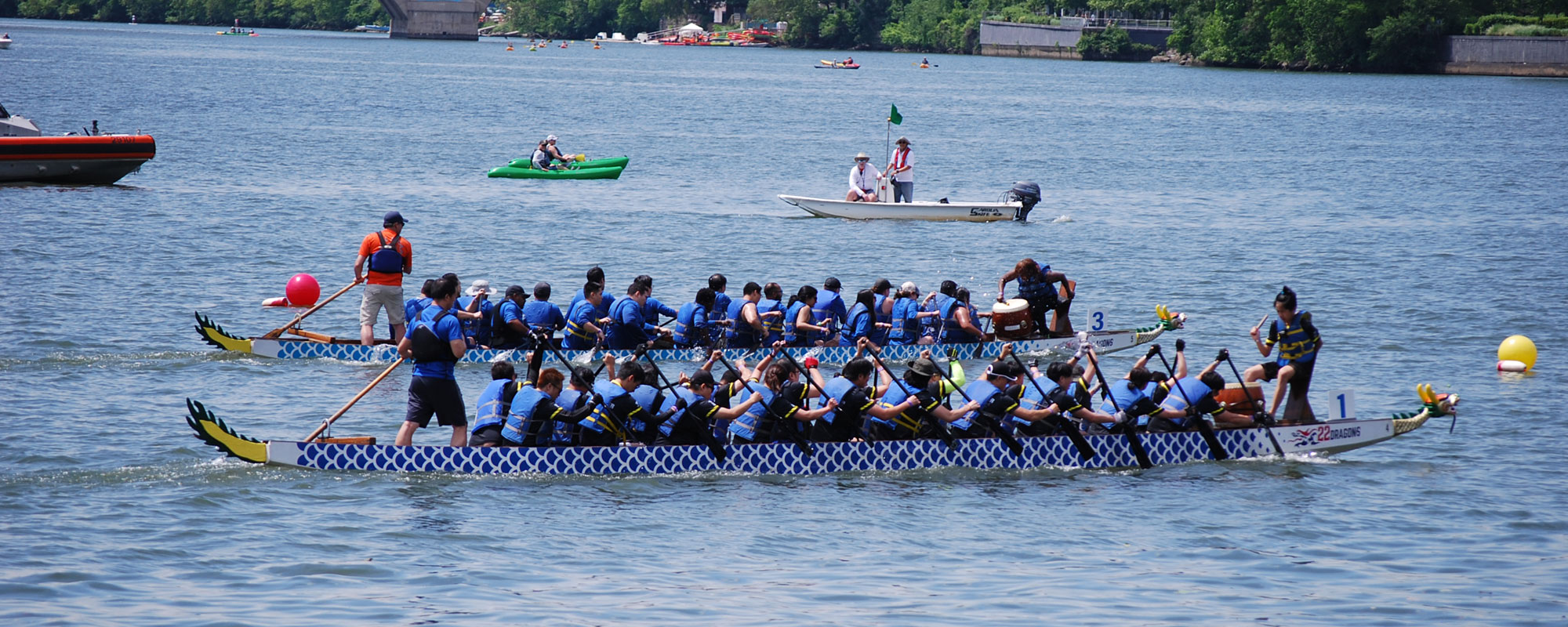 A dragon boat with 20 rowers is shown in silhouette as it moves along a river.