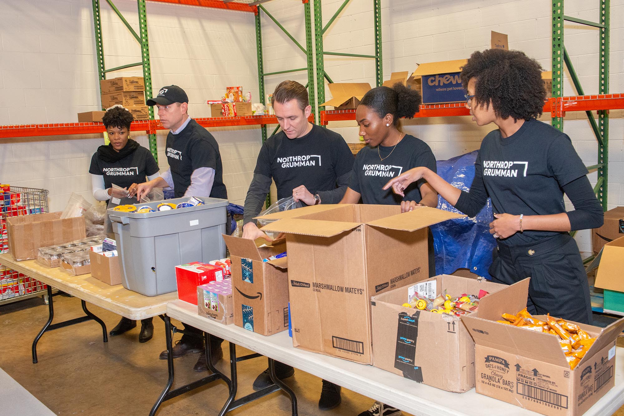 Several Northrop Grumman employee volunteers package food at a table