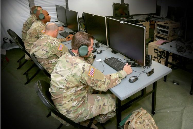 Army soldiers sit at desk on computers