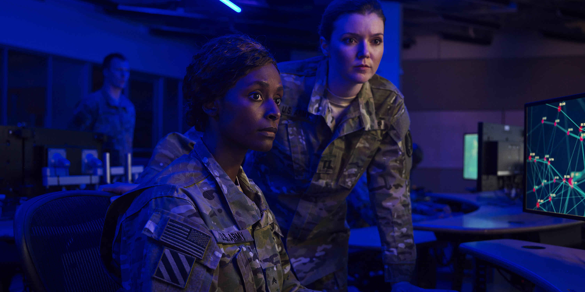 A black woman and a white woman in army suits in a control room.