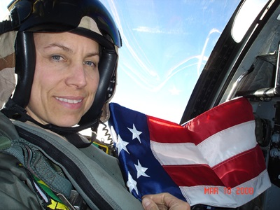 Female pilot in uniform, sitting in the cockpit with American flag in background