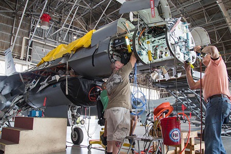 men working on front of military aircraft in hangar