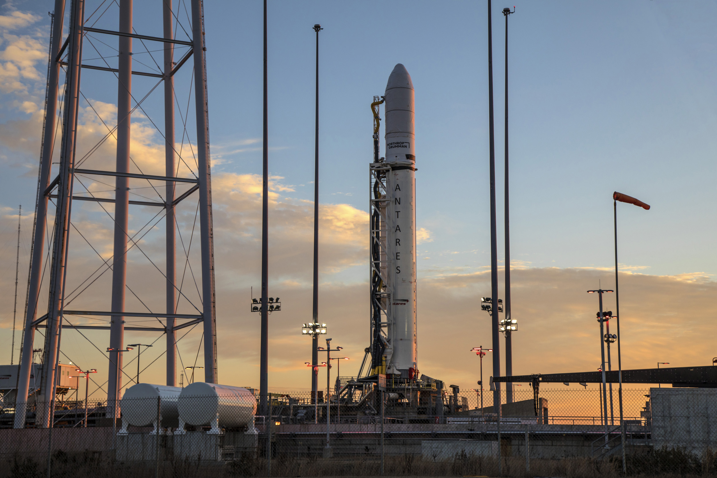 A rocket on launch pad at sunrise in front of a partial blue lit sky as sun comes up