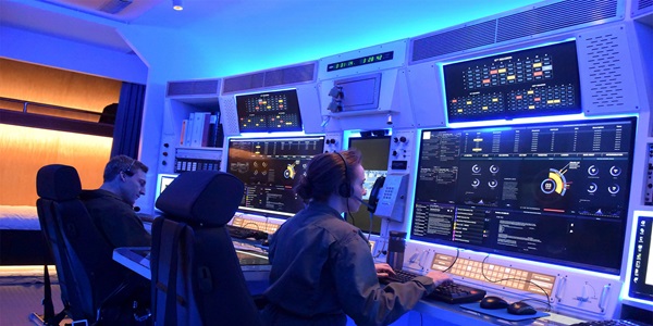 woman and man operating computers in a dark-lit control room