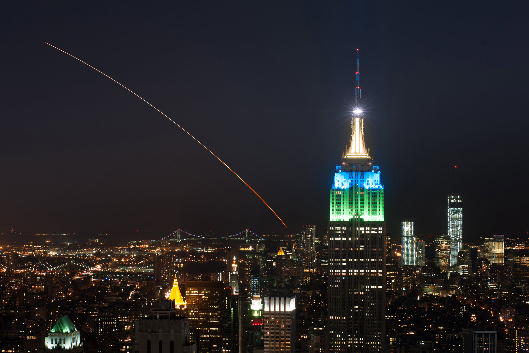 A rocket streak across the sky in New York City in front of the empire state building