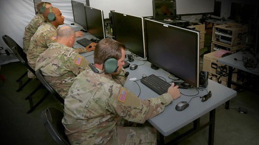 four men in military uniforms sitting at computer terminals