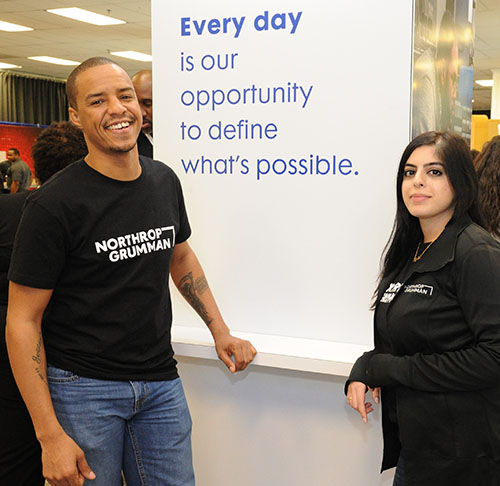 Man and woman in black Northrop Grumman shirts pose in front of banner
