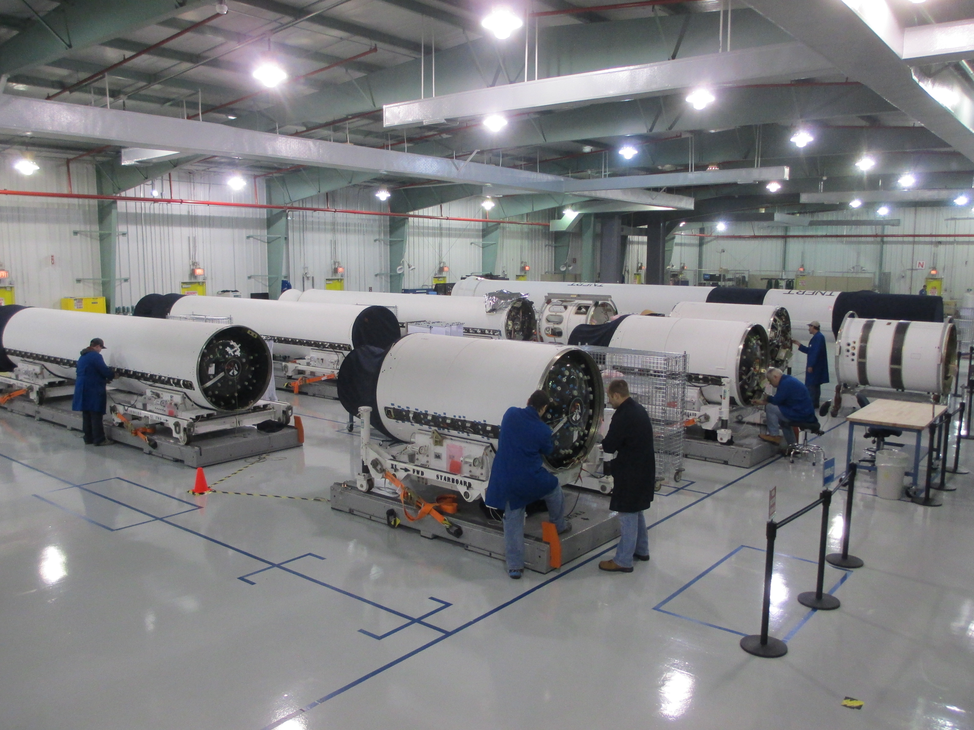 Employees in Facility wearing lab coats and working on large sections of rockets.