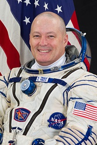 Bald man wearing astronaut uniform in front of American Flag