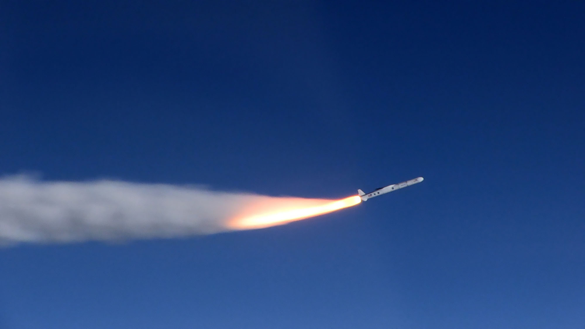 A rocket blasting off in blue sky with a plume