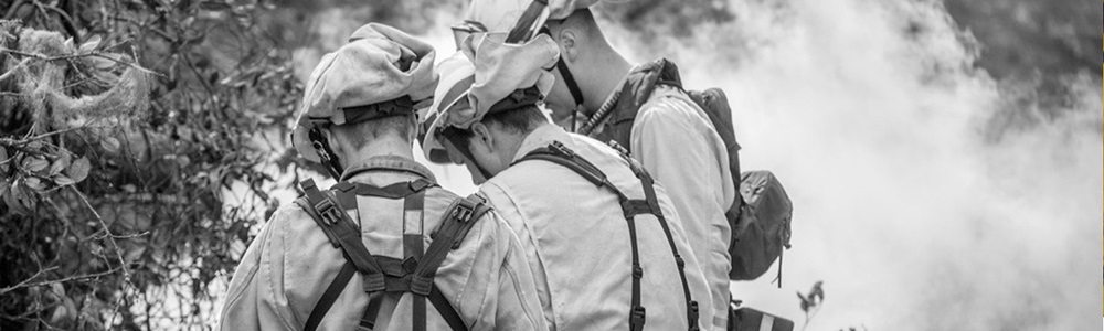 Black and white image of three firefighters gathered outside