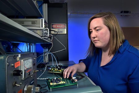 a white woman in a blue blouse works on a radio in a lab