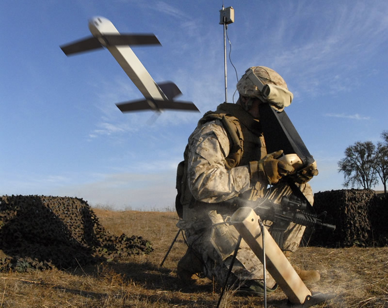 a soldier on the battlefield looks into a machine while an aircraft flies behind him