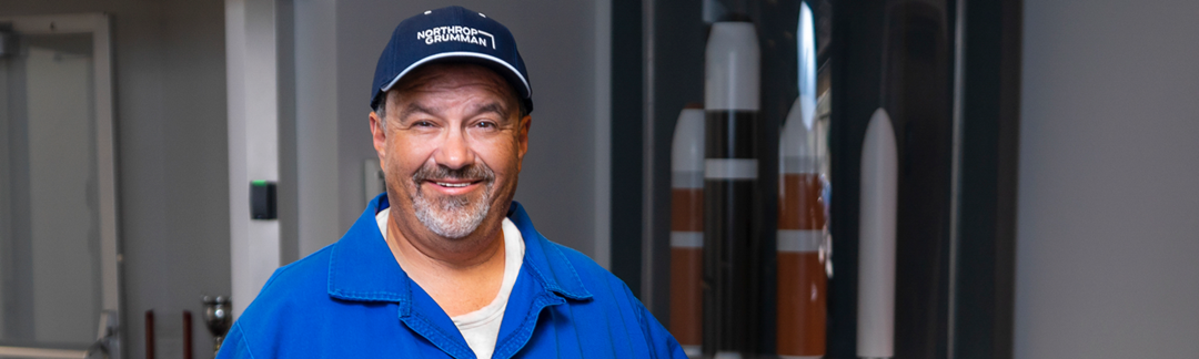 A Latino man in a blue work suit and hat