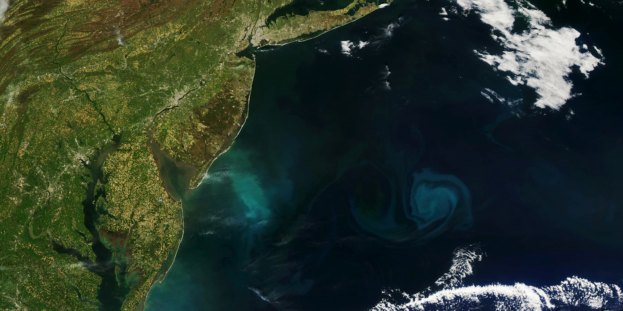 A satellite view of the Atlantic coast, with light green land and a turquoise blue ocean with white streaks.