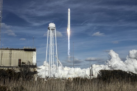 Rocket taking off from launch pad, with smoke rising from the ground in front of blue sky