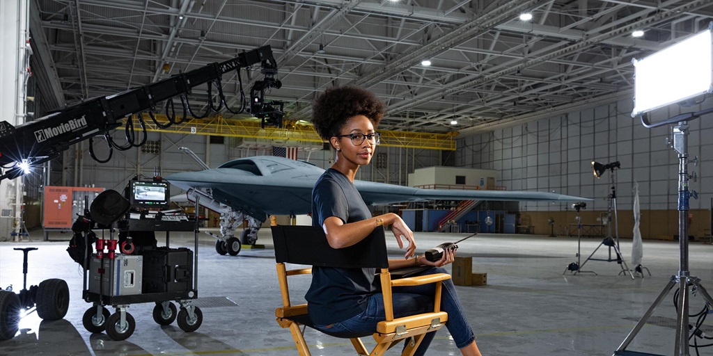 young black woman in director's chair in front of B-2 Bomber