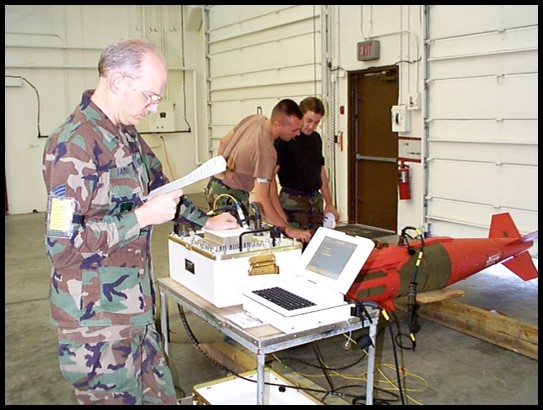 Service members in uniform work around desk of equipment