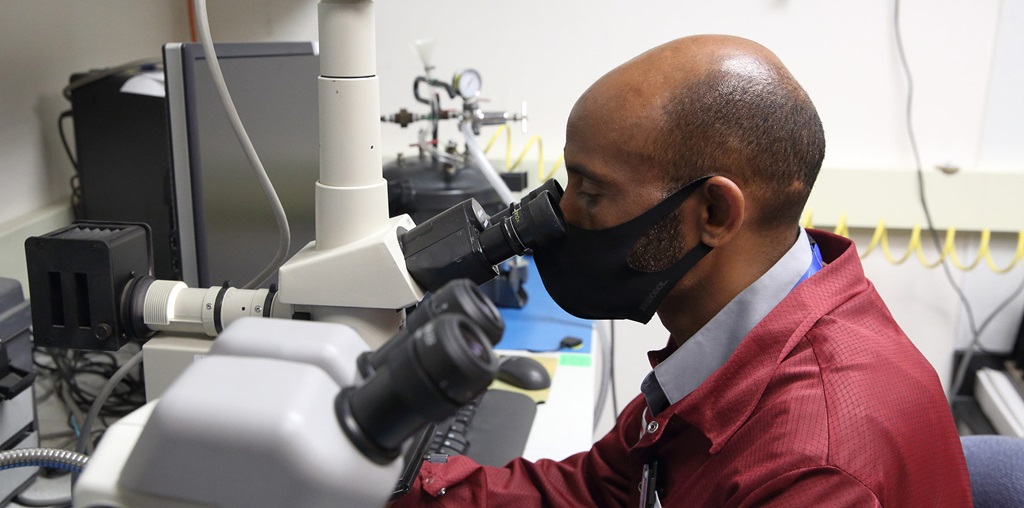 a man in a maroon lab coat looks into a telescope