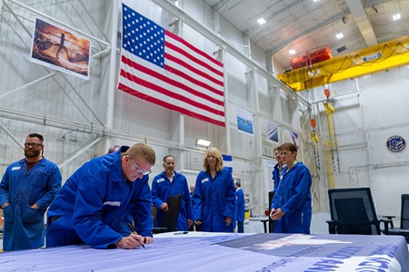 people in blue overalls signing banner in manufacturing facility