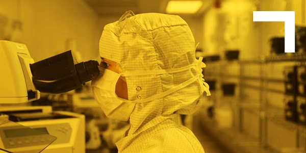 woman in clean room looking through microscope