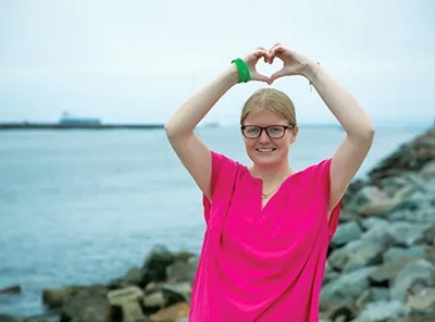 woman in pink shirt with hands making a heart