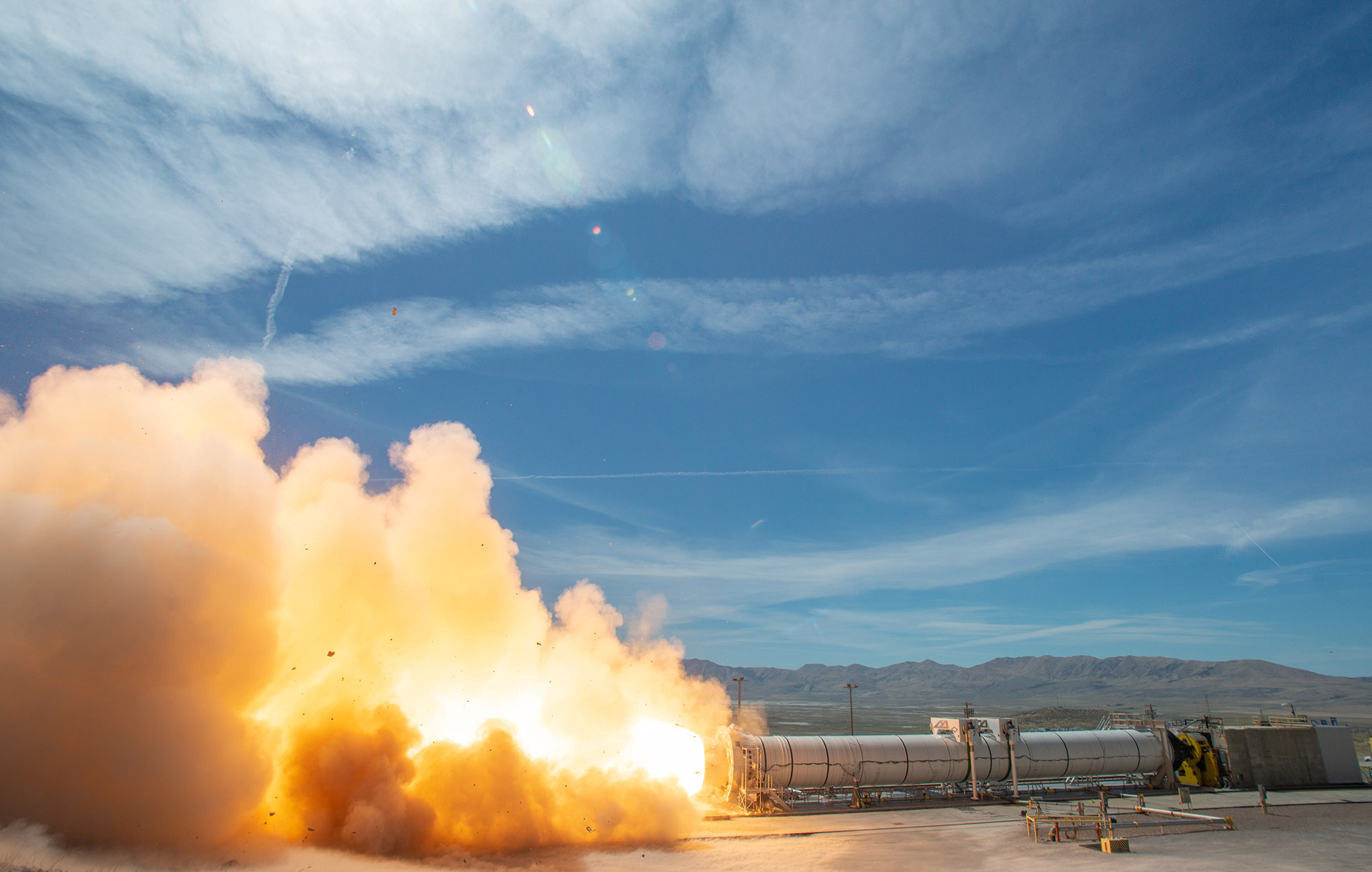A rocket motor test firing at test site in front of mountains and blue sky