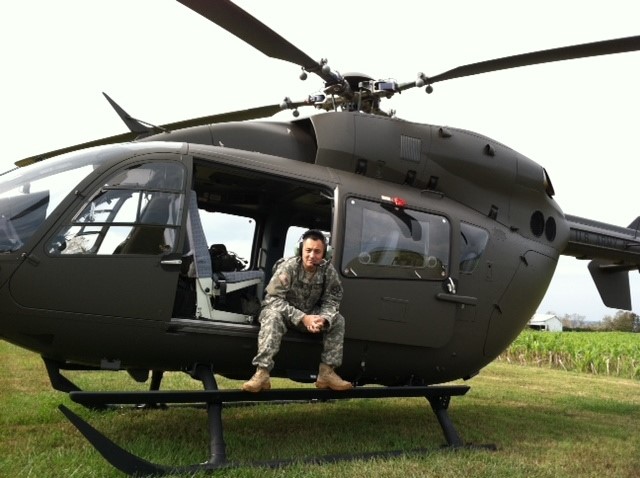 Man in military uniform sitting in open door of helicopter on ground