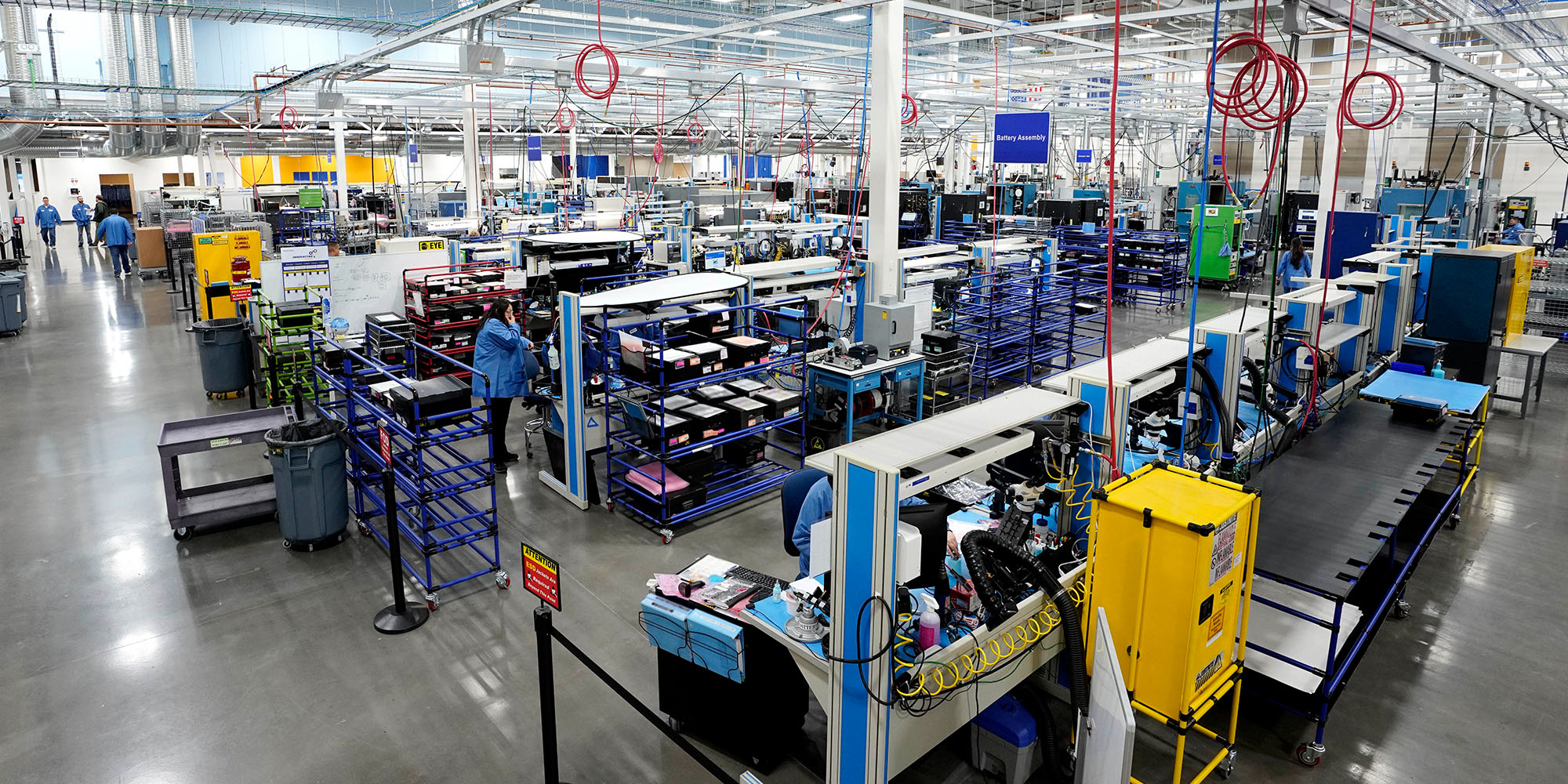 A large manufacturing plant floor with people in blue lab coats and large manufacturing machines