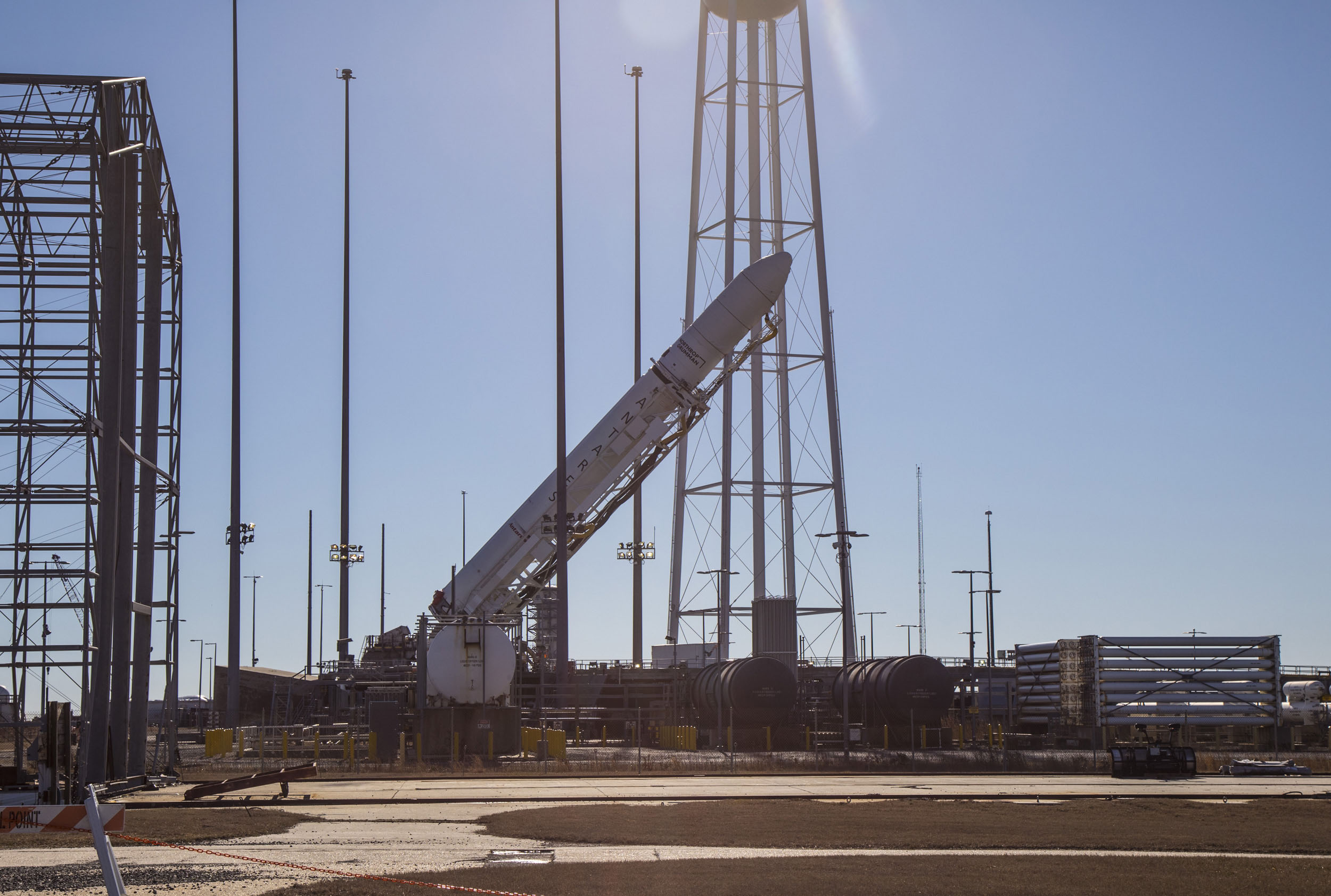 A rocket tilted sideways on launch pad as it is being placed in launch postion in front of a blue sky