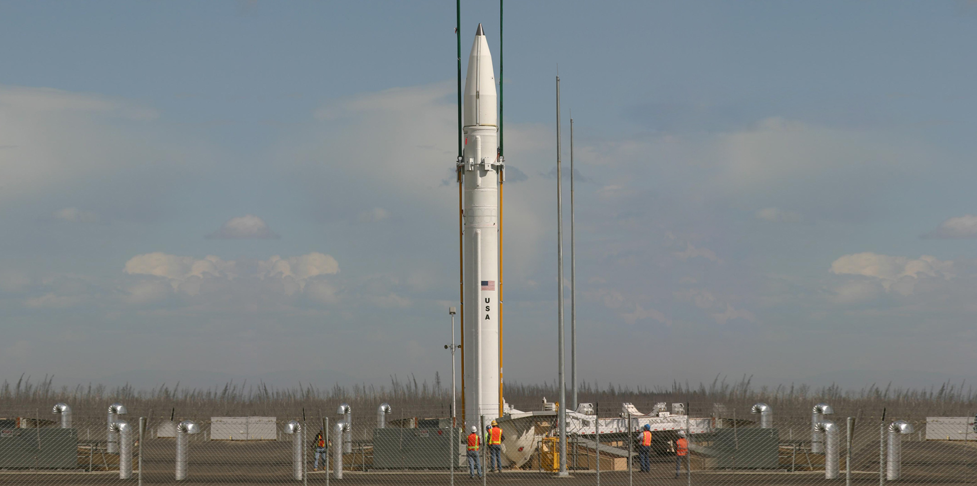 A white missile interceptor on a launchpad in front of blue light cloudy sky