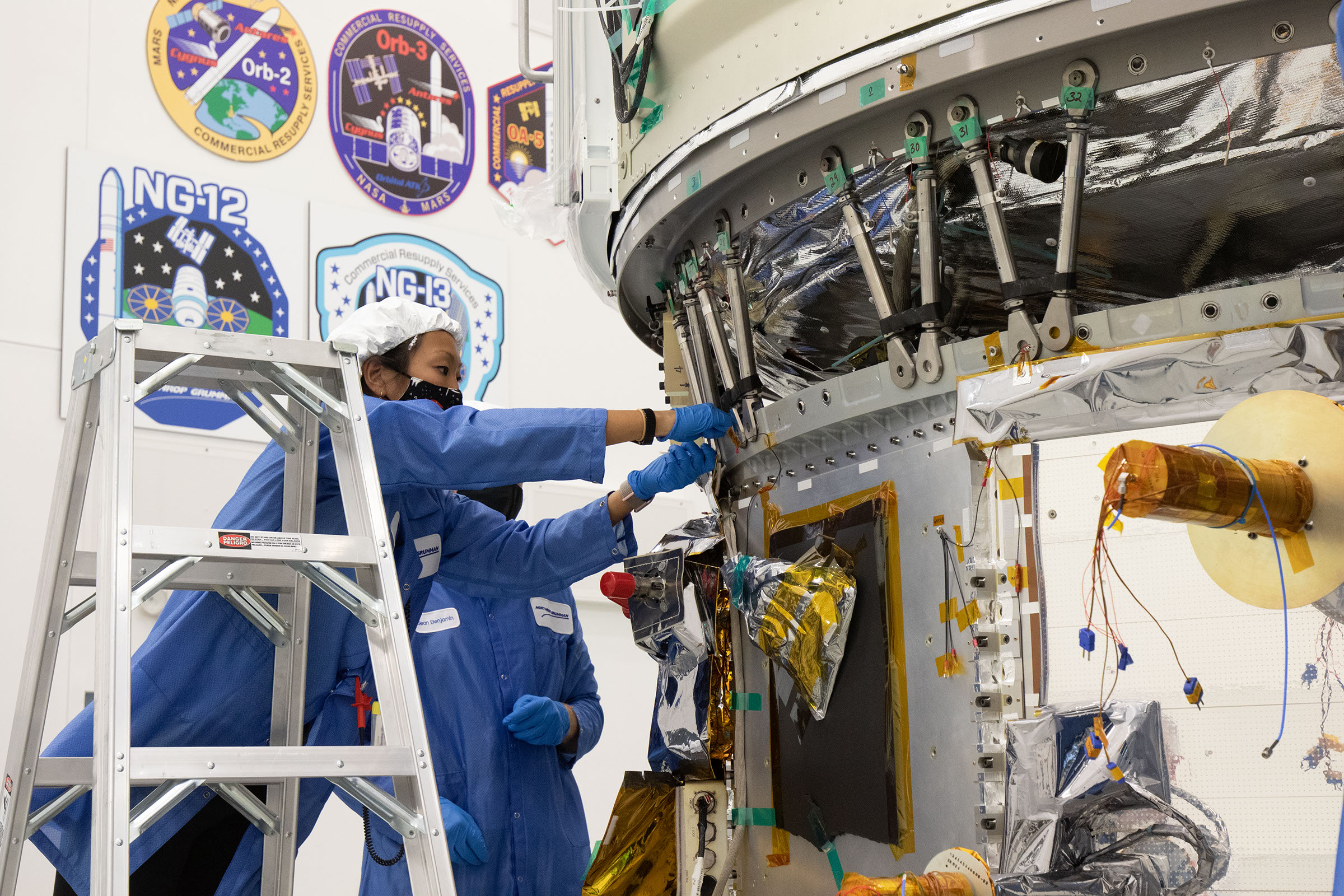 Asian engineer on ladder assembles parts to Cygnus Space Craft in Wallops Island flightfacility